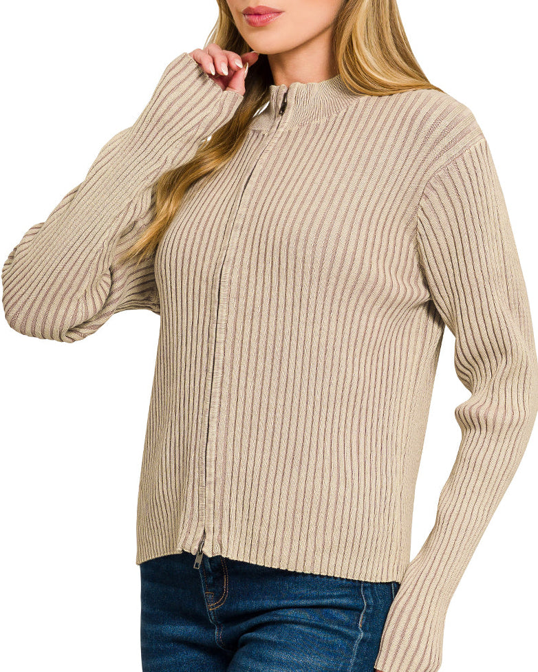 Woman wearing a light mocha ribbed zip up sweater over a white top and blue jeans on a white background.