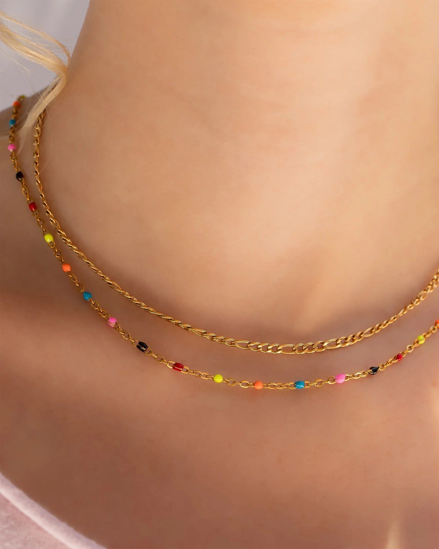 Gold chain necklace with colorful beads on a person's neck.