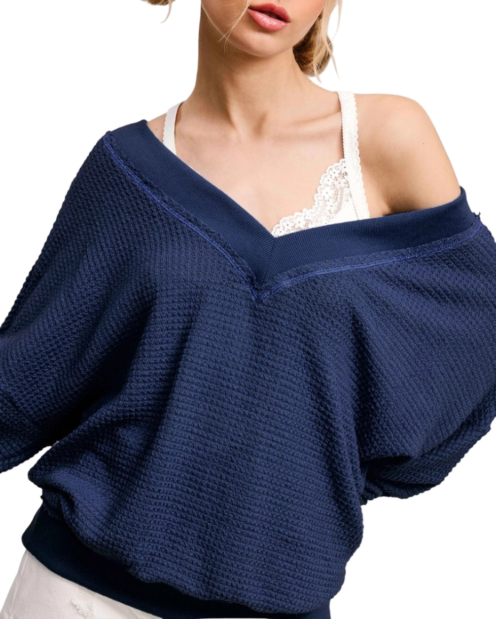 Woman wearing a navy blue oversized dual V sweater over a white top.