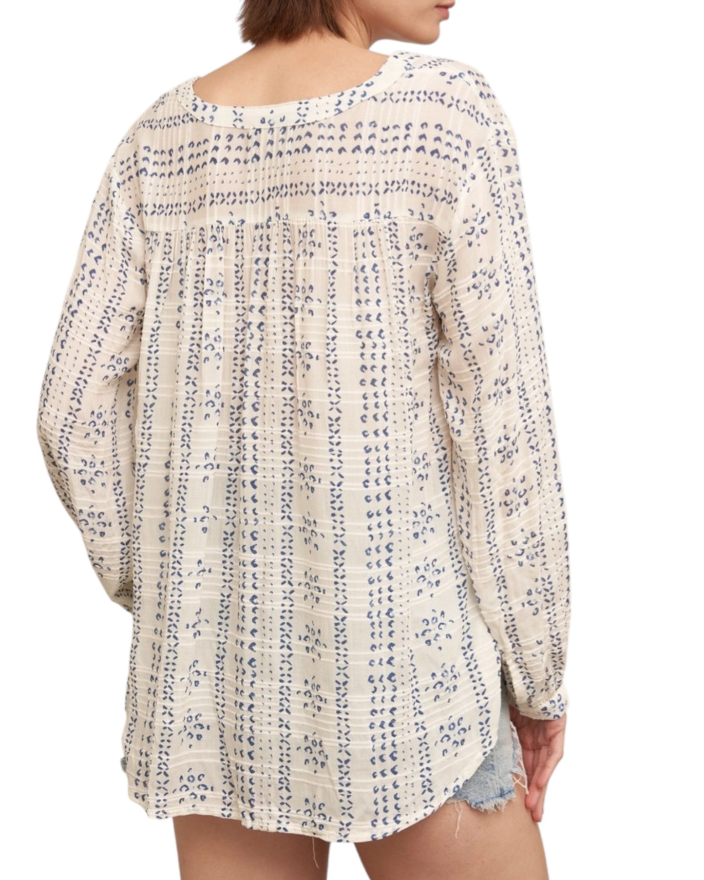 Woman wearing a textured ivory blouse with blue print and denim shorts on a white background.