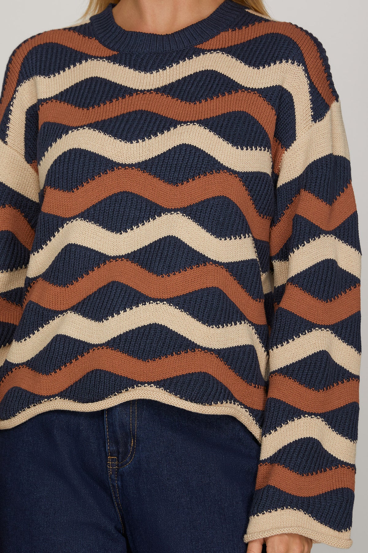 Close-up of ivory, navy, and cinnamon wave stripe knit sweater showing textured stitching, ribbed crew neckline, and rolled hem.
