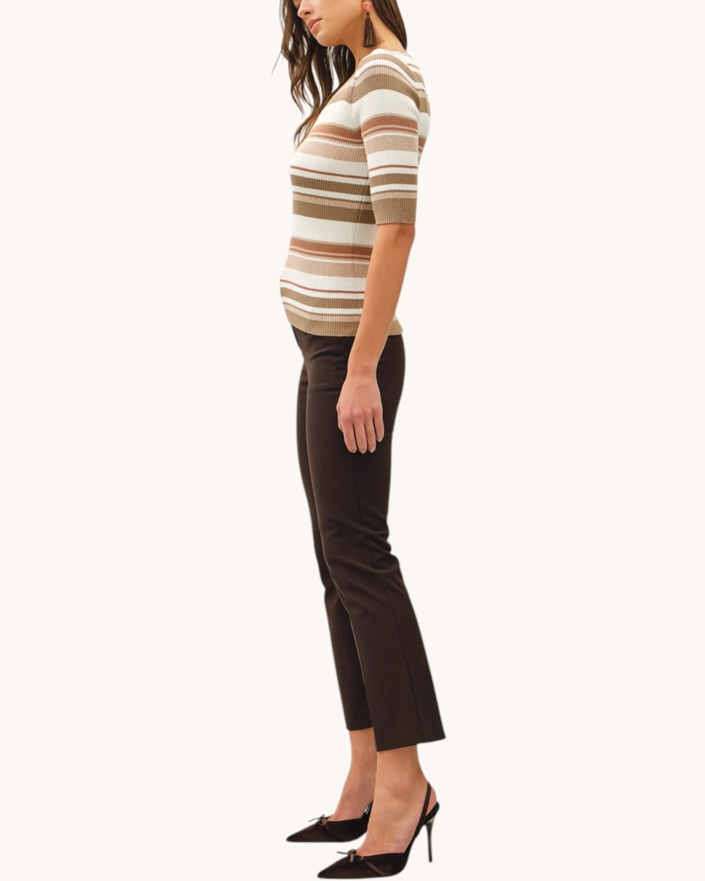 Woman wearing a striped shirt in warm earth tones and black pants and heels on a white background.