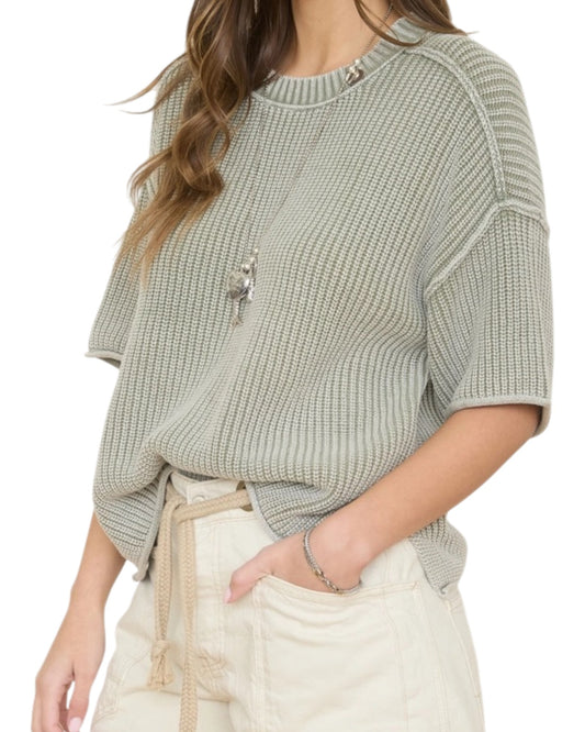 Woman wearing a light green washed short sleeve knit sweater on a white background.