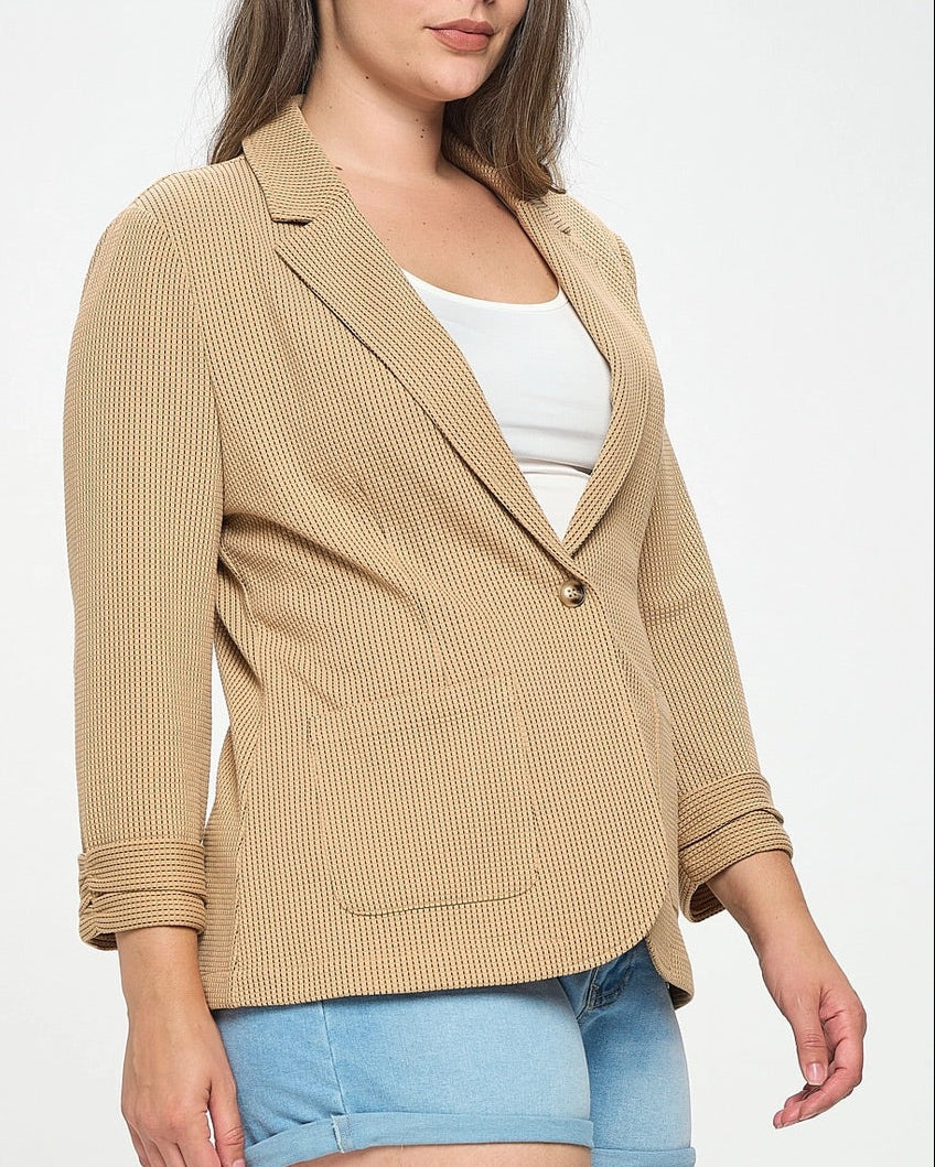 Woman wearing a beige blazer over a white top and blue shorts on a white background.