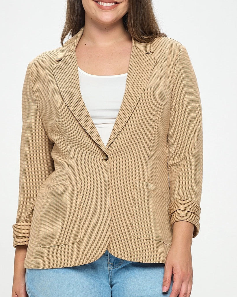 Woman wearing a beige blazer over a white top and blue shorts on a white background.