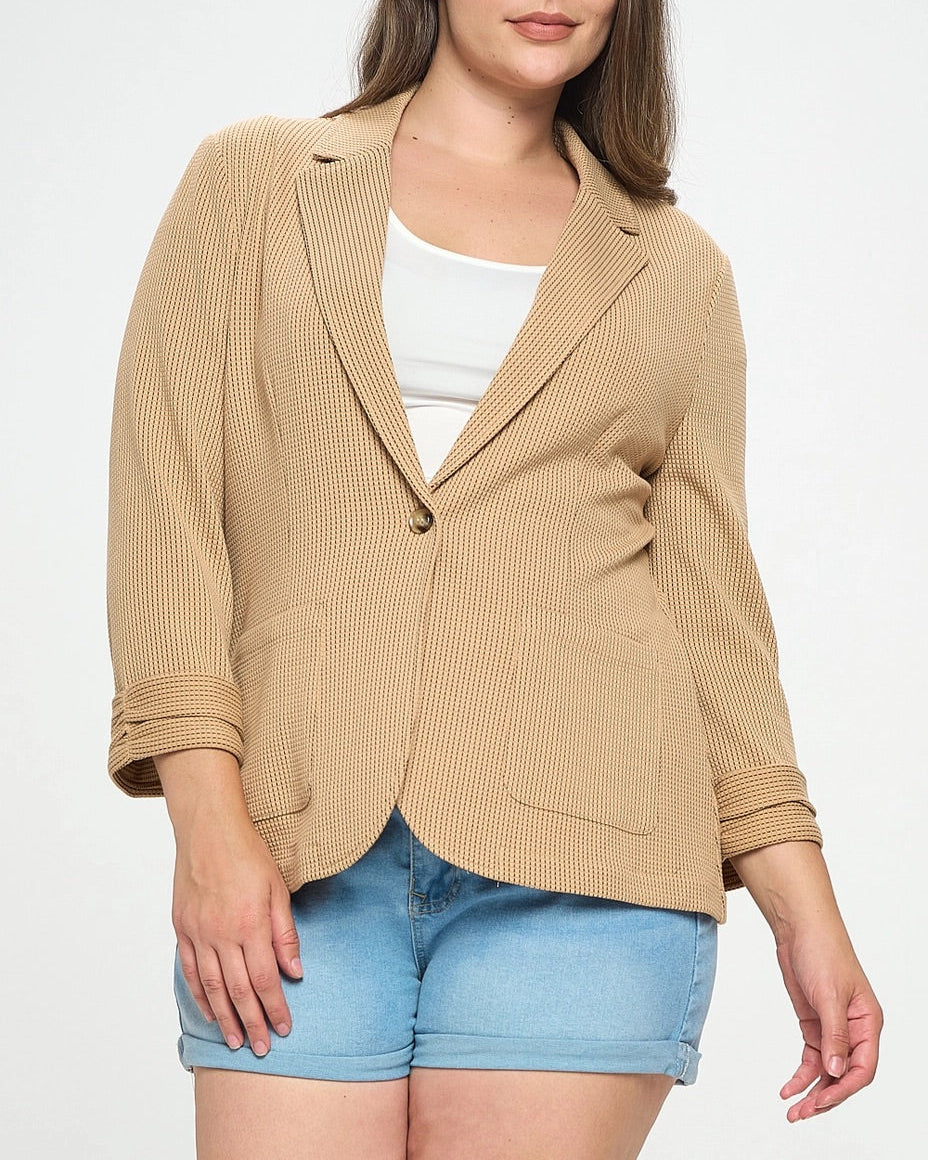 Woman wearing a plus-size beige blazer over a white top and blue shorts on a white background.