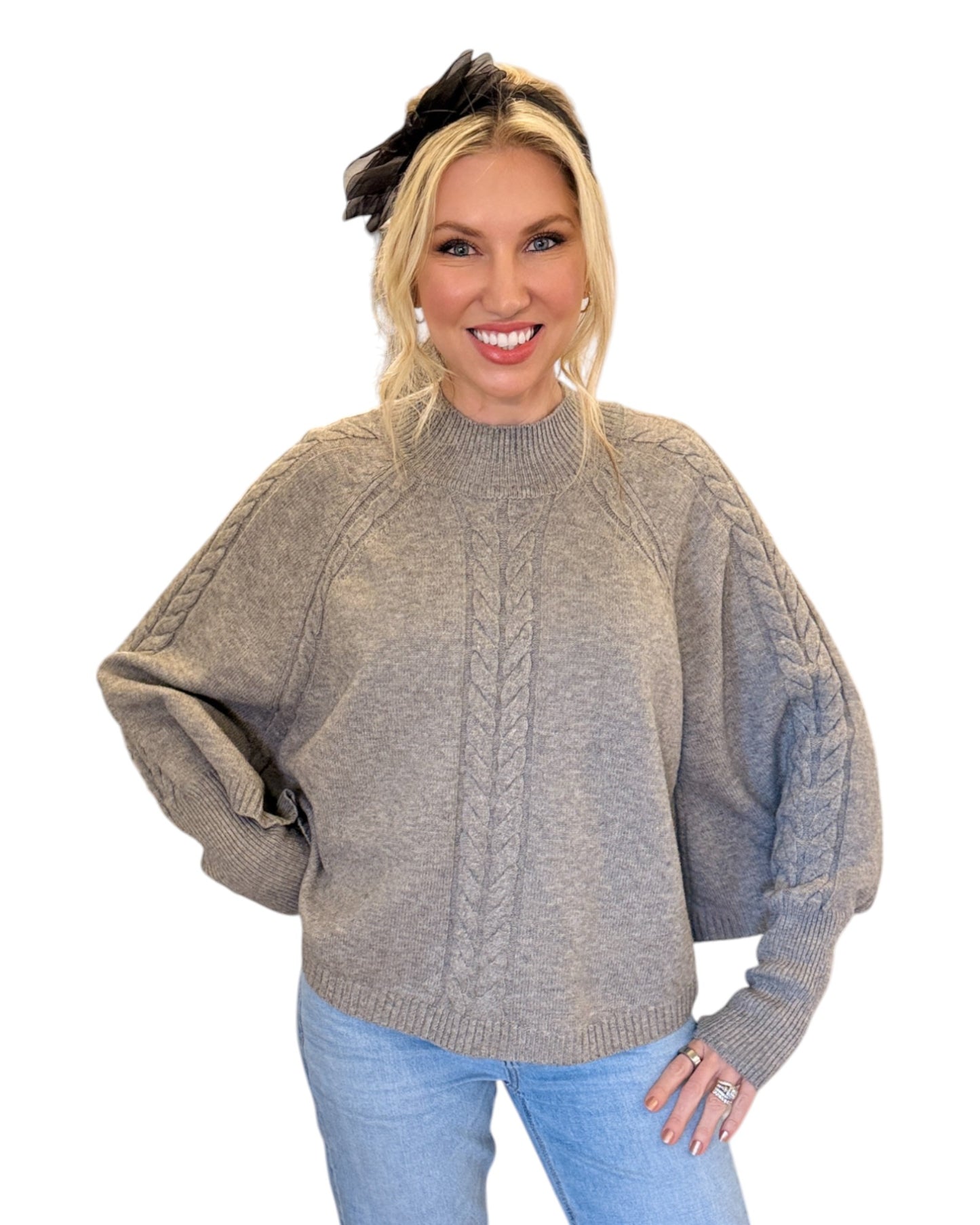 Woman wearing jeans and a Heather Grey/Taupe Cable Knit Mock Neck Poncho with a relaxed silhouette, cable knit design, and fitted sleeve hem, perfect for cozy layering.