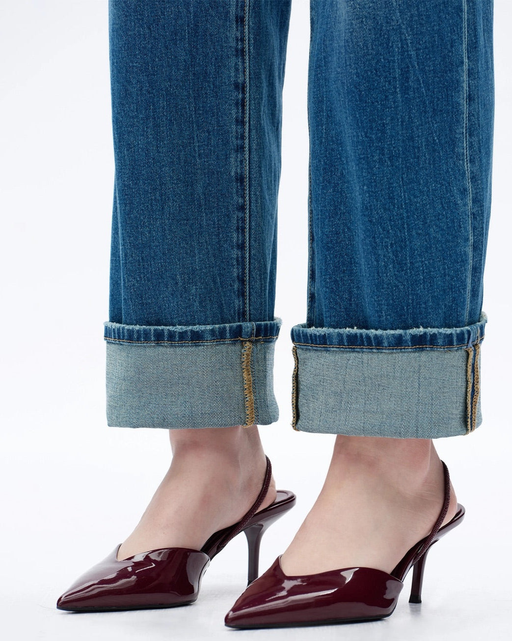 Cuffed blue jeans with burgundy high-heeled shoes on a white background.