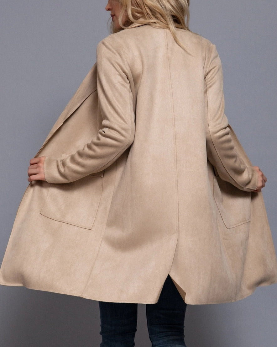 Woman wearing a beige coat against a gray background.