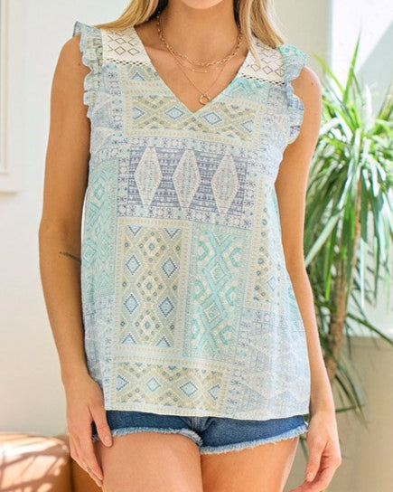 Woman wearing a green, blue and ivory geometric patterned sleeveless top and denim shorts.