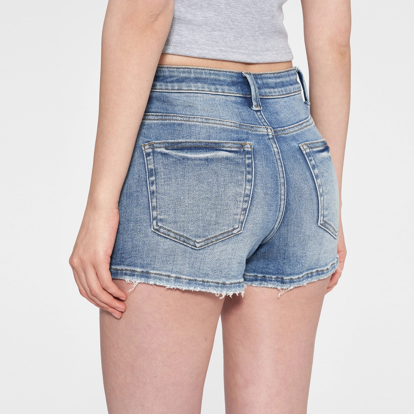 Woman wearing high-rise medium blue denim shorts with distressed details and a raw hem.