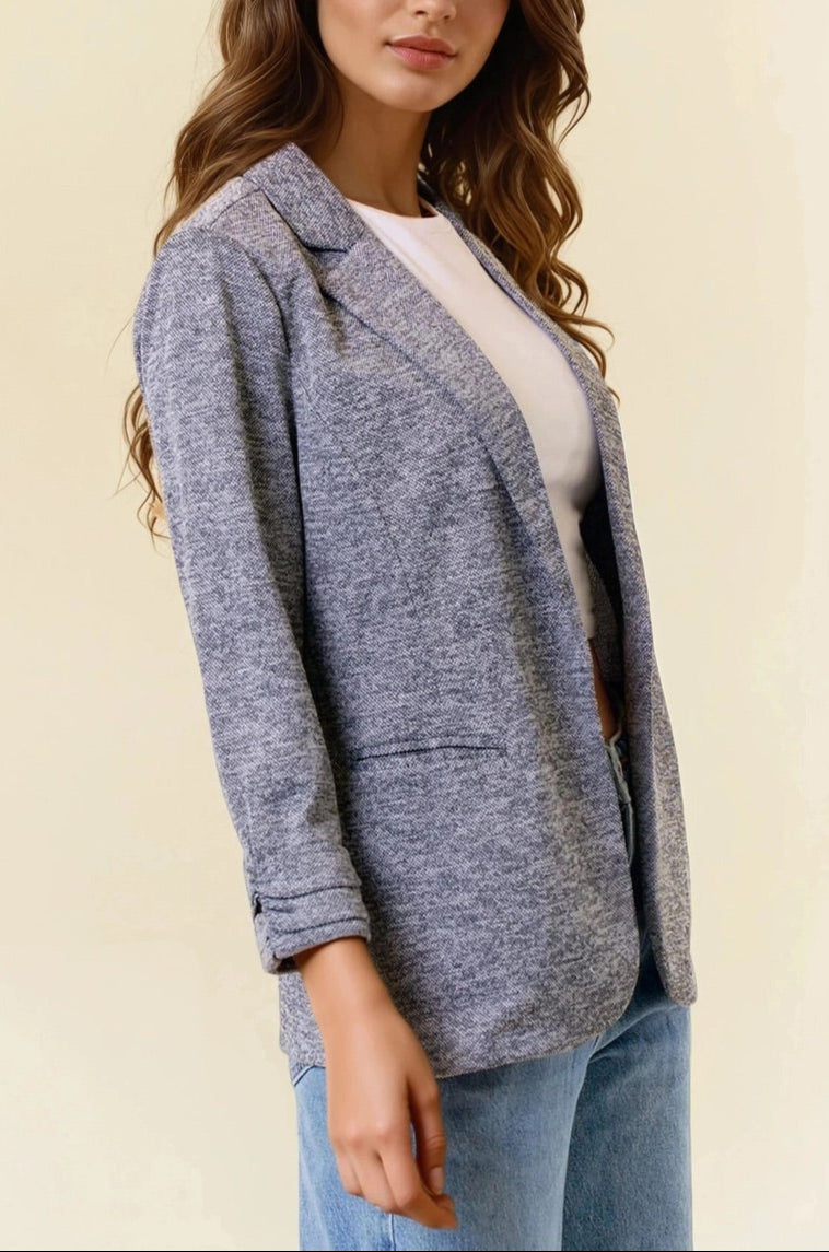 Woman wearing a charcoal blazer over a white top and blue jeans on a beige background.