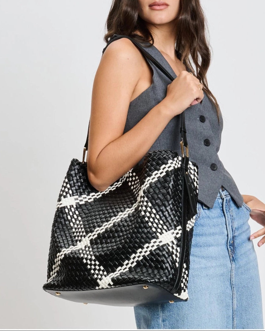 Woman holding a black and white plaid woven vegan leather handbag against a plain background.