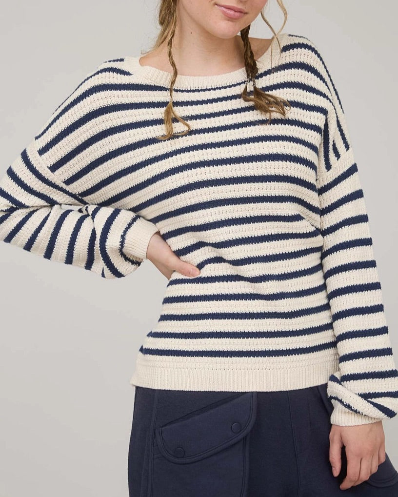 Woman wearing a navy and white striped long sleeve sweater with navy pants against a plain background.