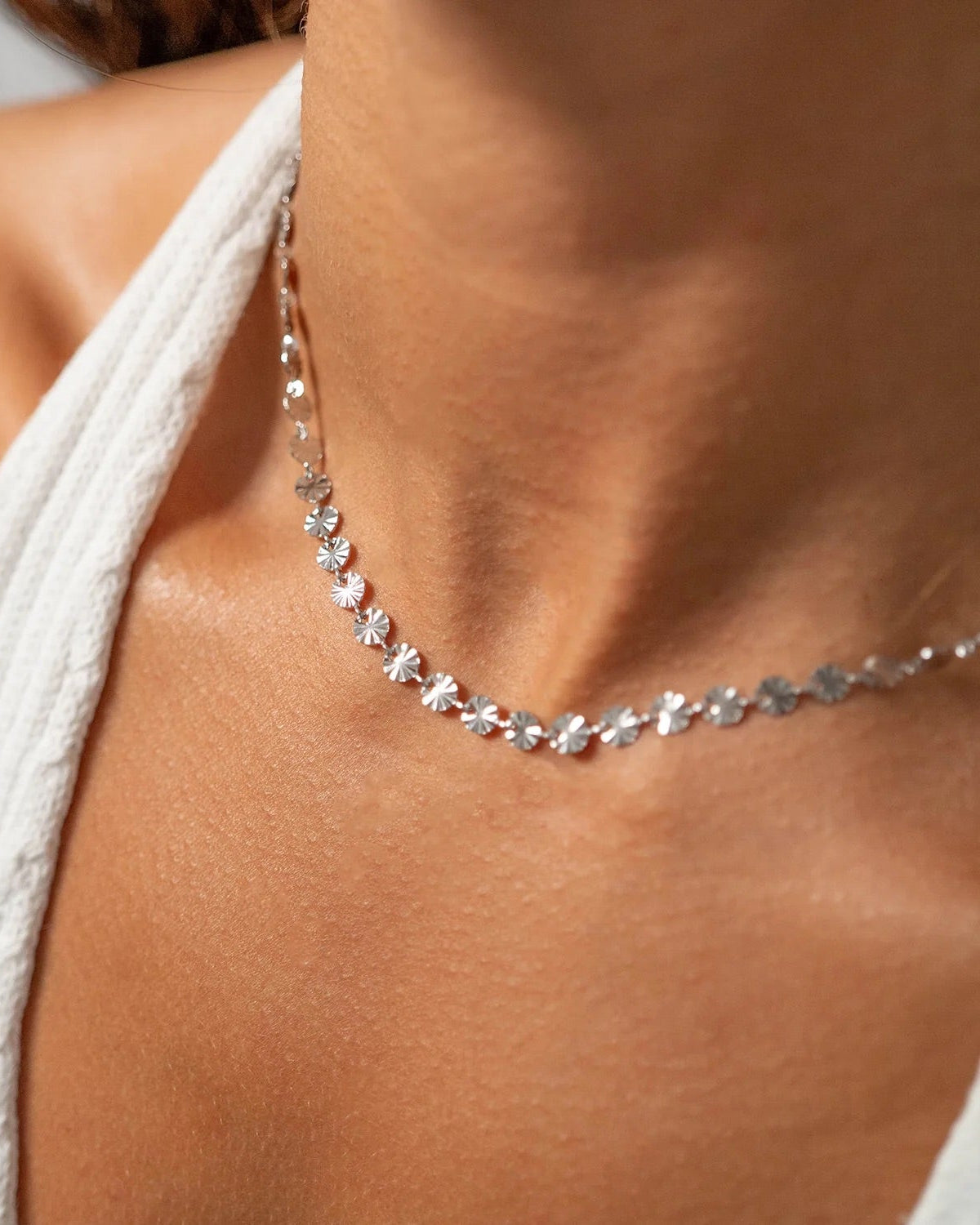 Close-up of a silver sunburst necklace on a person wearing a white top.