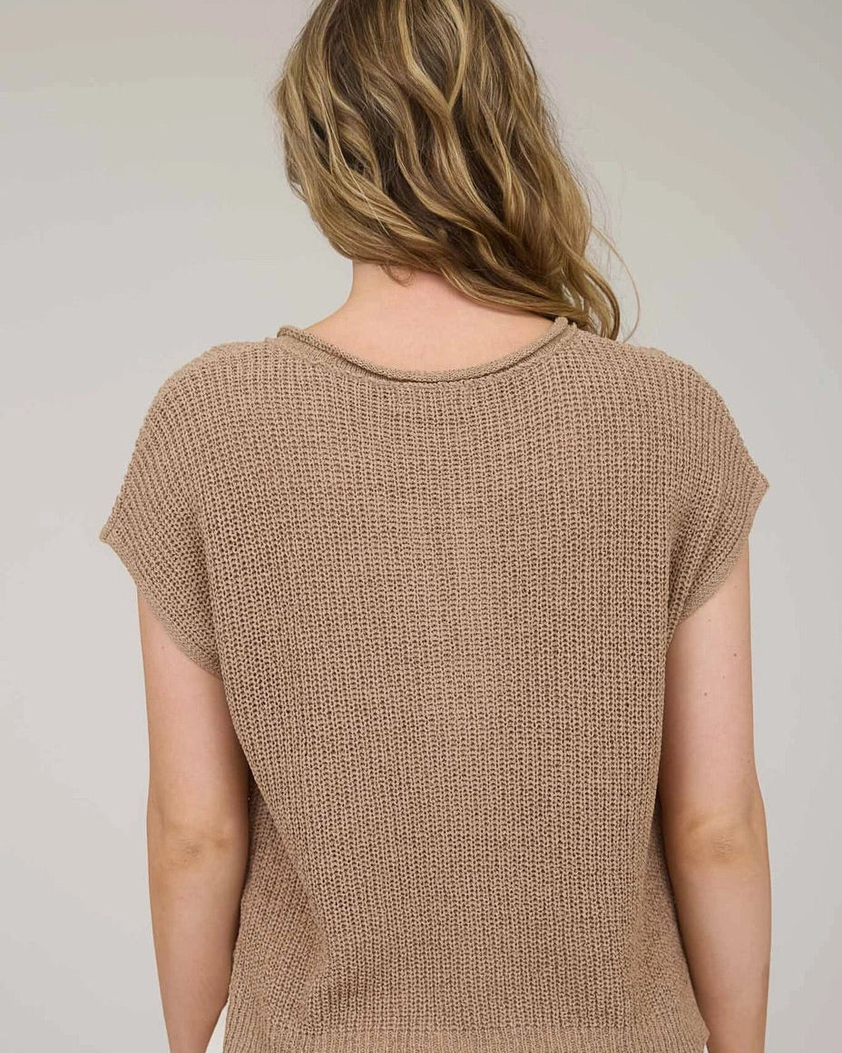 Woman wearing a tan knitted top against a plain background.