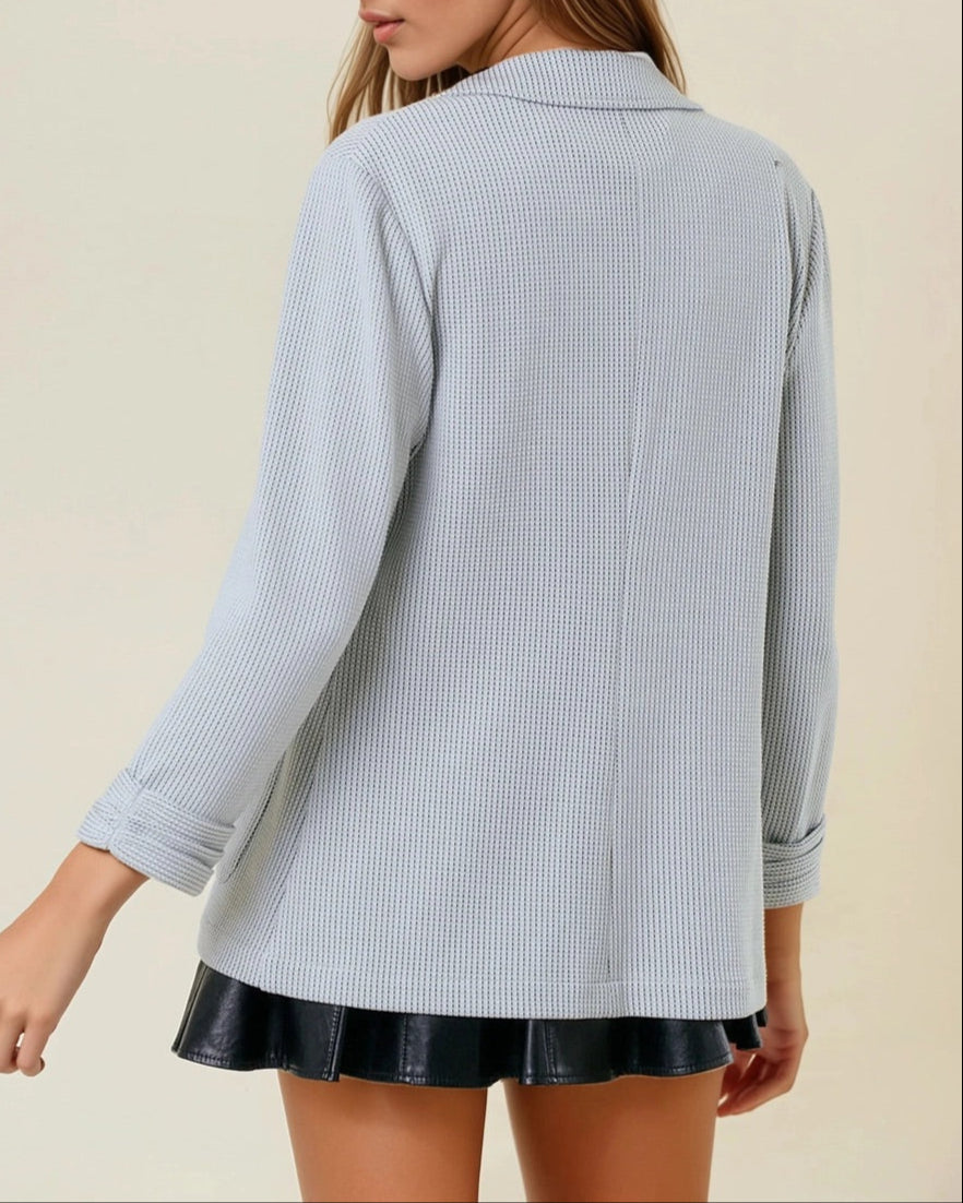 Woman wearing a grey textured blazer over a white top and black skirt on a beige background.