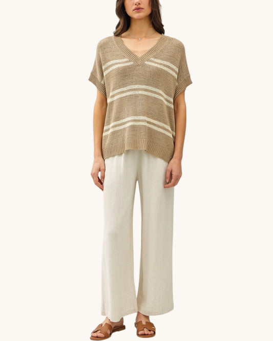 Woman wearing a brown and white striped sweater with white pants on a white background.