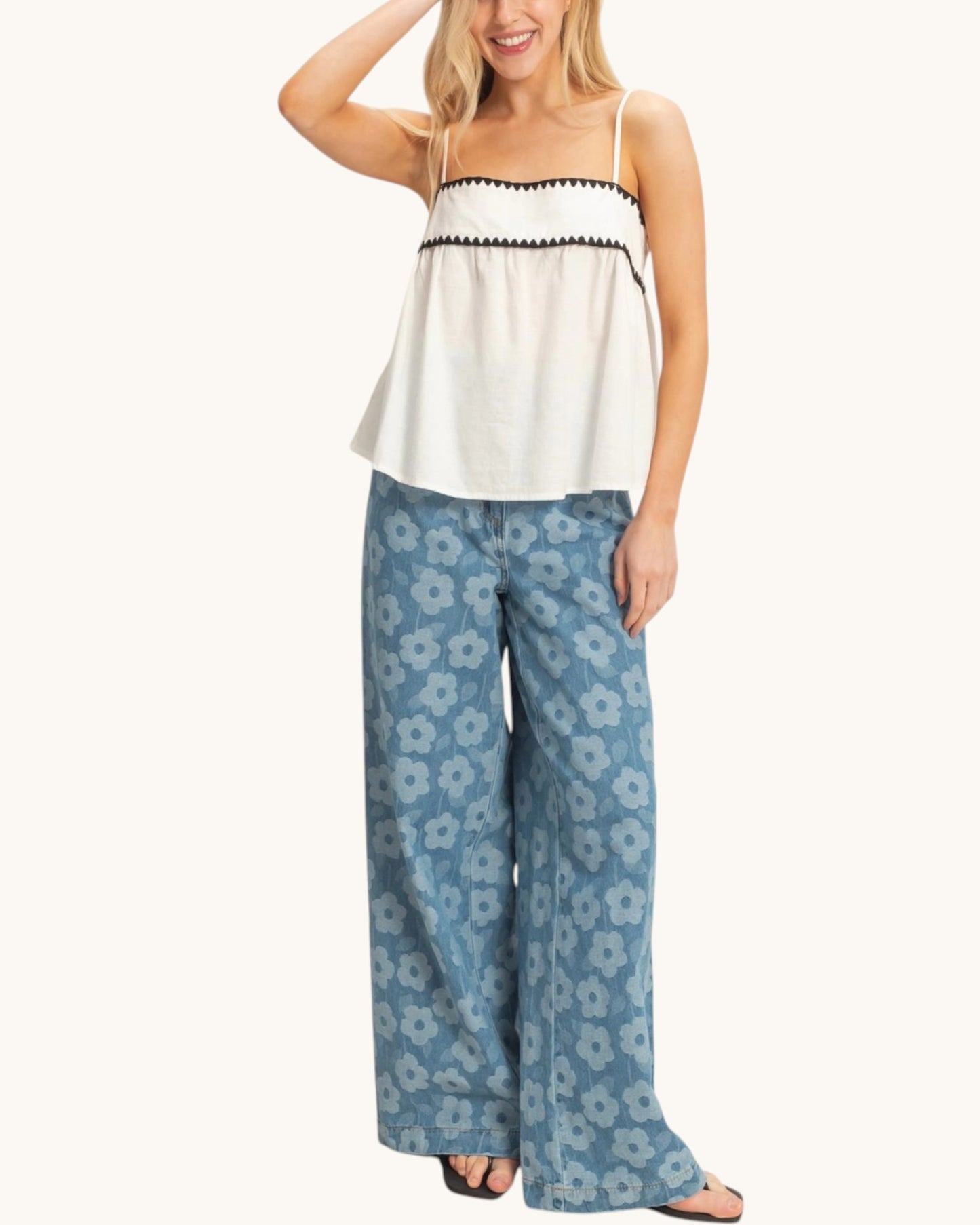 Woman wearing a white top and blue floral pants on a white background.