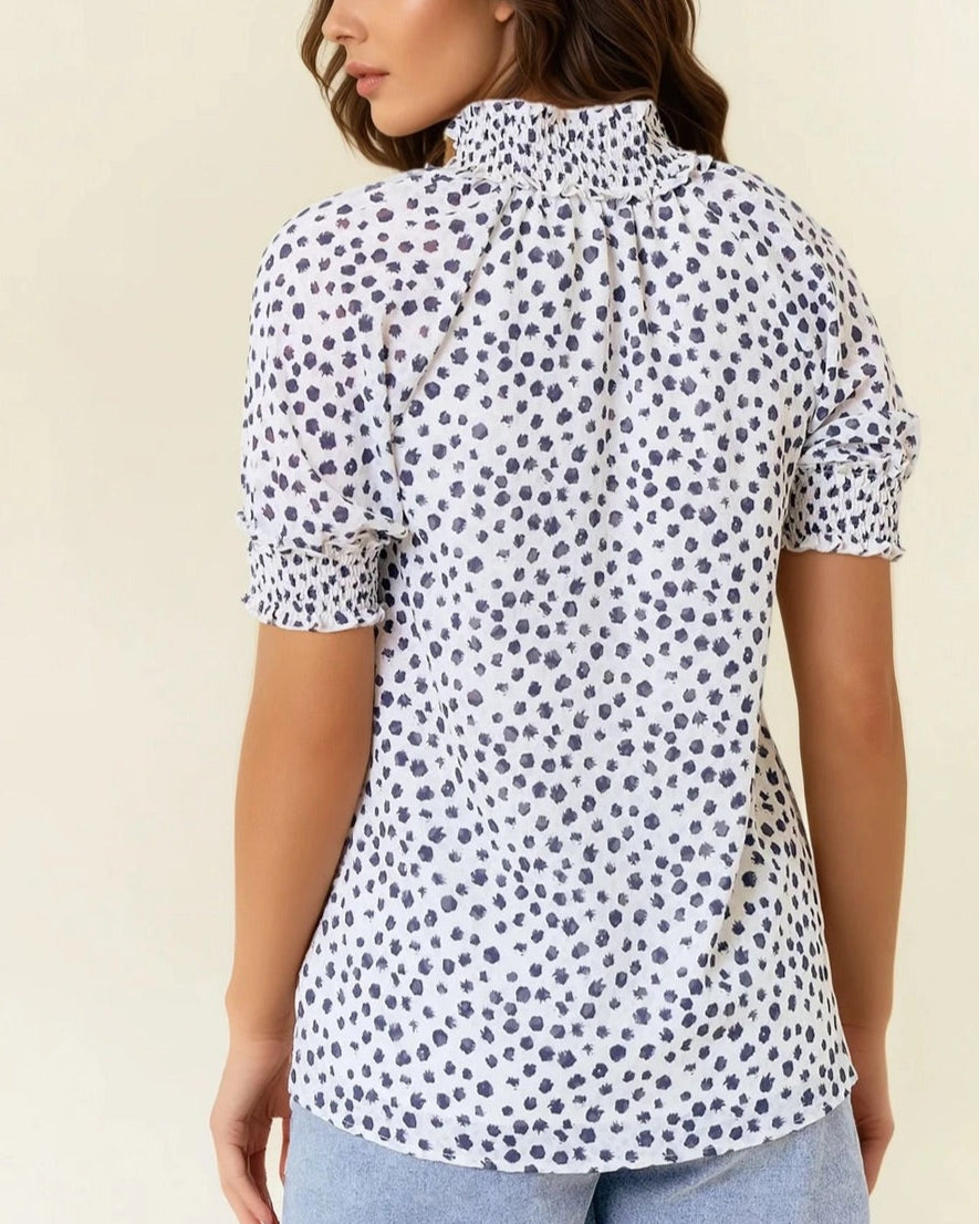 White short sleeve blouse with navy dot print and ruffled neck.