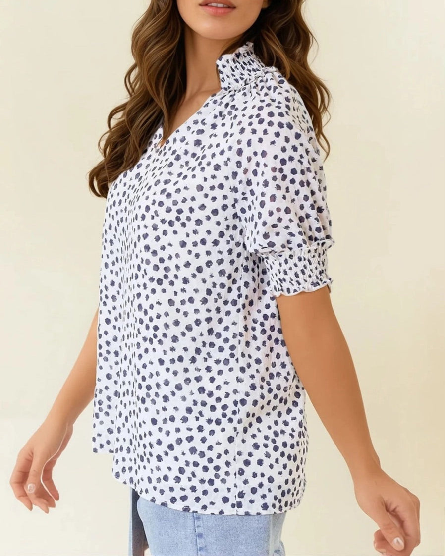 White short sleeve blouse with navy dot print and ruffled neck.