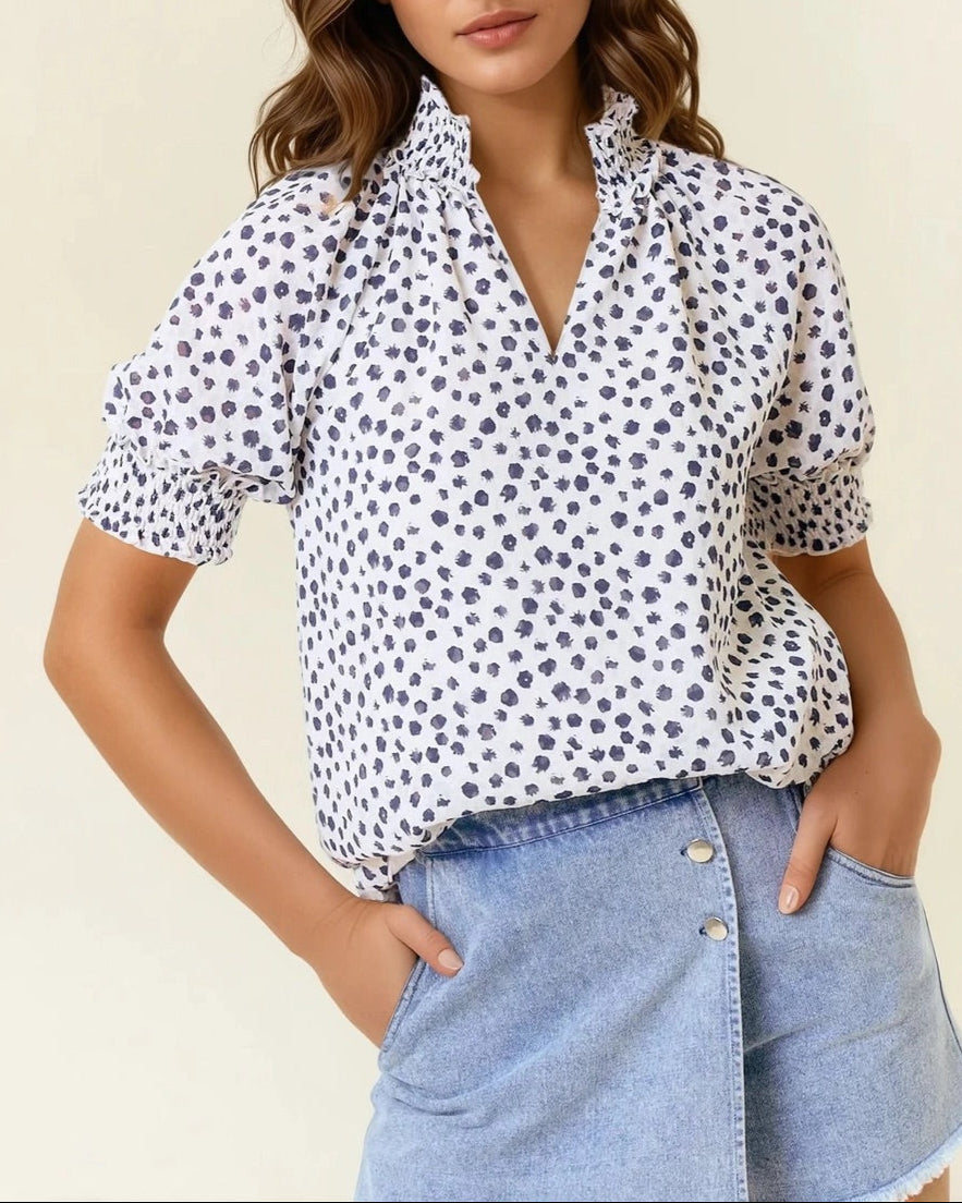 White short sleeve blouse with navy dot print and ruffled neck.