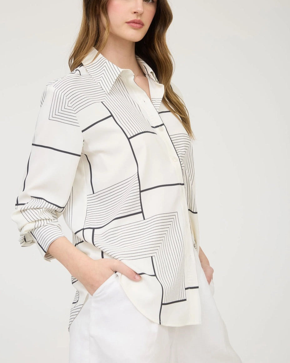 Woman wearing a white shirt with black geometric patterns on a plain background.