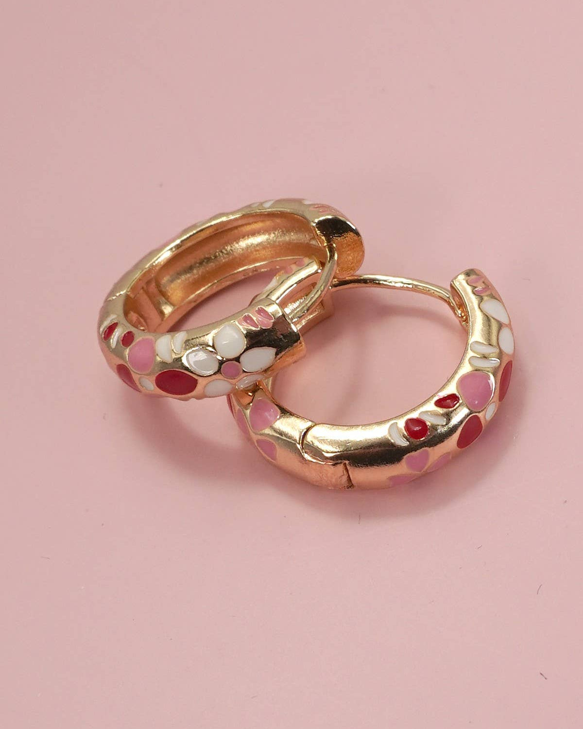 Gold hoop earrings with colorful accents on a pink background.