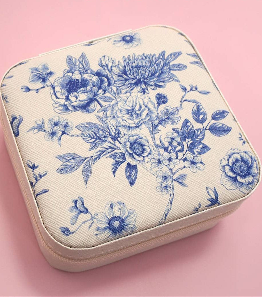 An off-white zippered case with a blue floral toile de Jouy pattern, shown on a solid pink background.