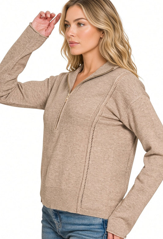 A woman modeling a heathered taupe quarter-zip pullover sweater with decorative vertical stitching, paired with blue jeans against a plain white background.