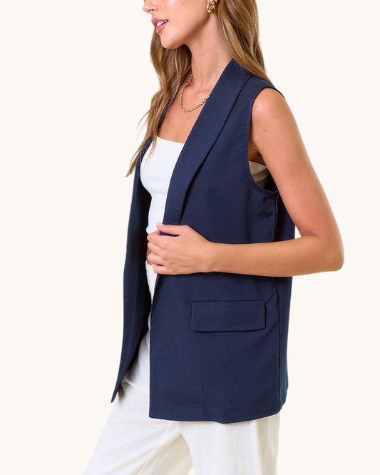 Woman wearing a navy blue sleeveless blazer over a white top on a white background.