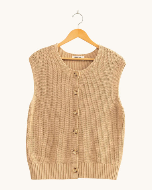 A sleeveless ribbed knit cardigan vest in a warm beige/tan color, hanging on a wooden hanger against a plain off-white background.
