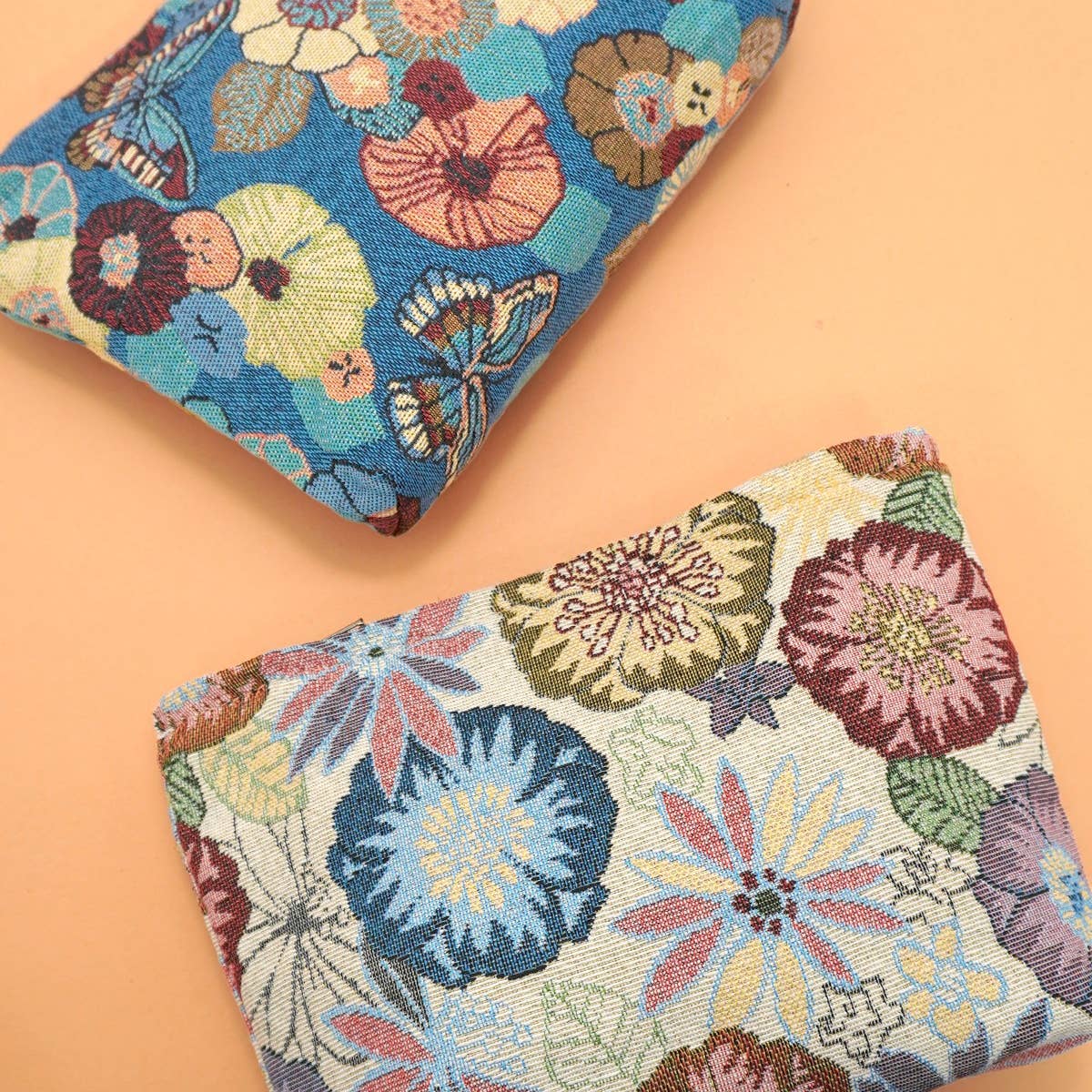 Two floral embroidered make-up pouches on a peach background.