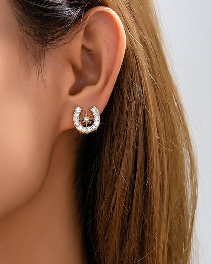 Close-up of an woman wearing a crystal horseshoe and star stud earring with a neutral background.