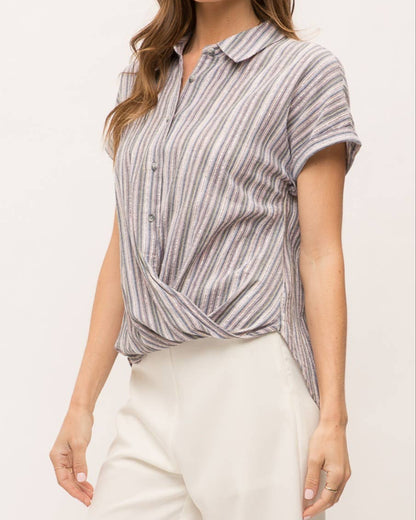 Woman wearing striped short sleeve button-up shirt with wrap front drape, collar and gold lurex detail.