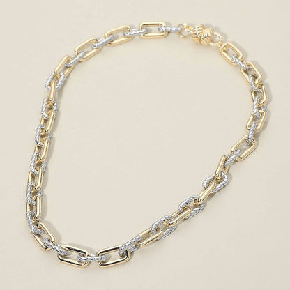 Gold and silver chain statement necklace on a beige background.
