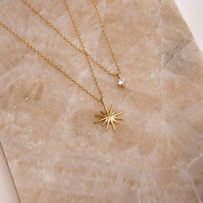 Gold necklace with a star-shaped pendant and a CZ stone on a beige marble surface.