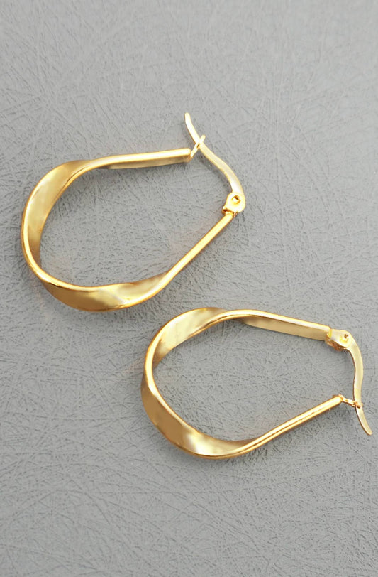 A pair of gold-toned, twisted oval hoop earrings with leverback closures, displayed on a textured gray background.