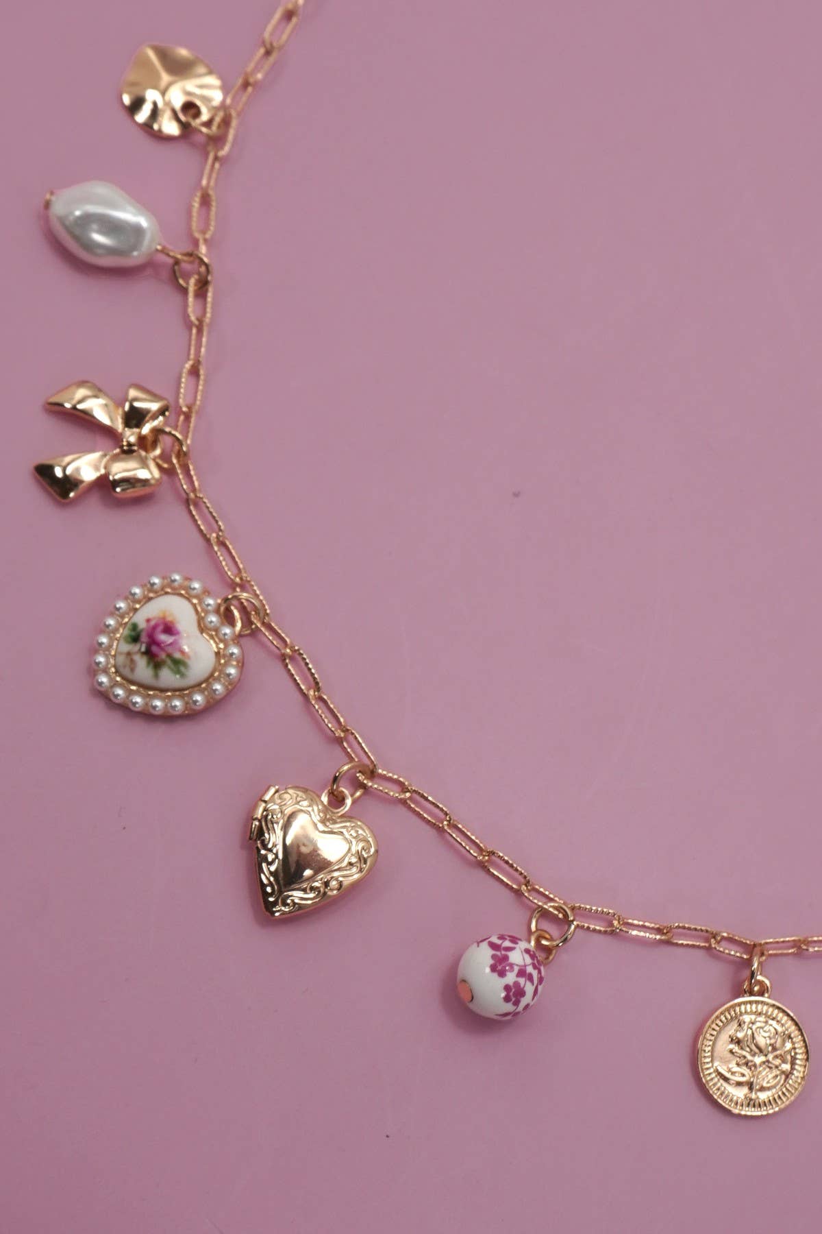 Gold necklace with various charms on a pink background.