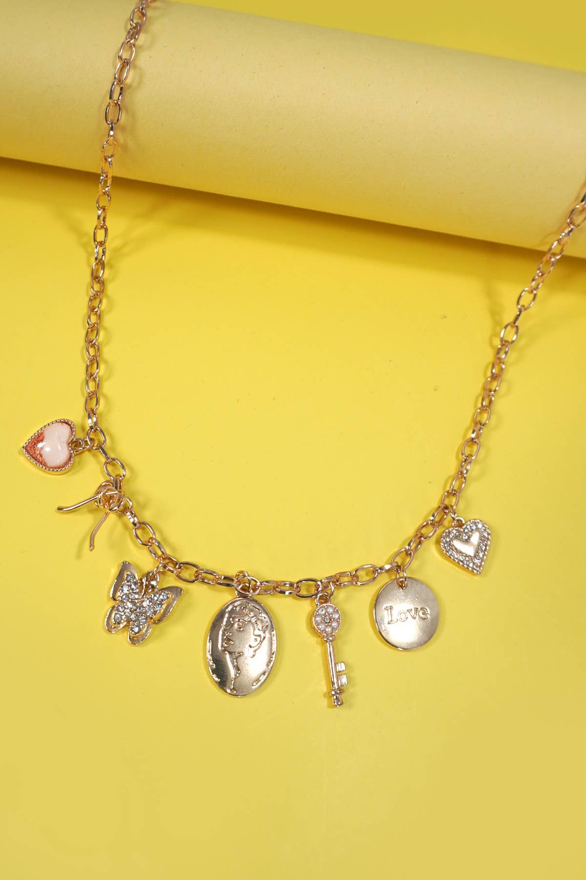 Gold charm necklace with a bow, heart, key, butterfly, and sparkling rhinestone accents.