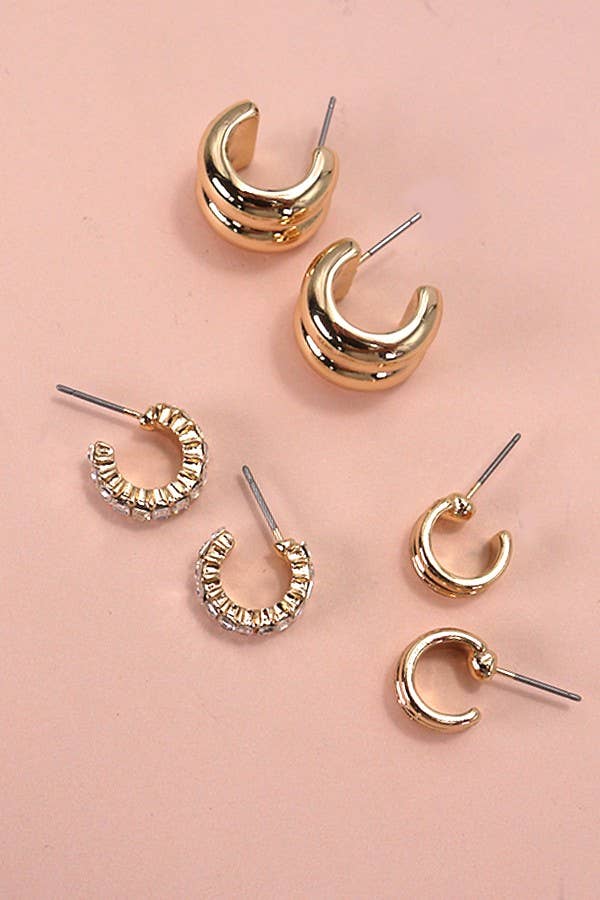 Set of gold huggie hoop earrings on a pink background.