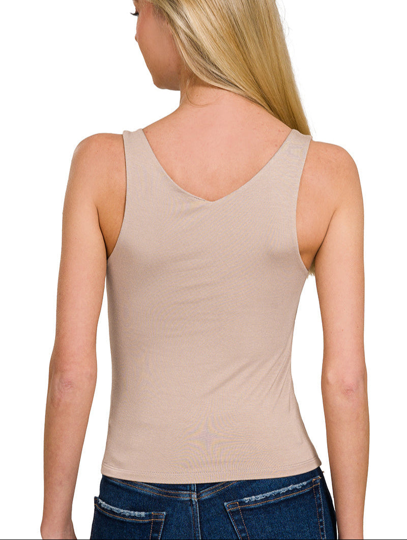 Woman wearing a beige tank top and blue jeans on a white background.