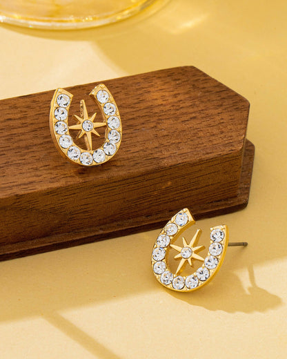 Gold earrings with star and horseshoe design on a wooden stand against a yellow background.