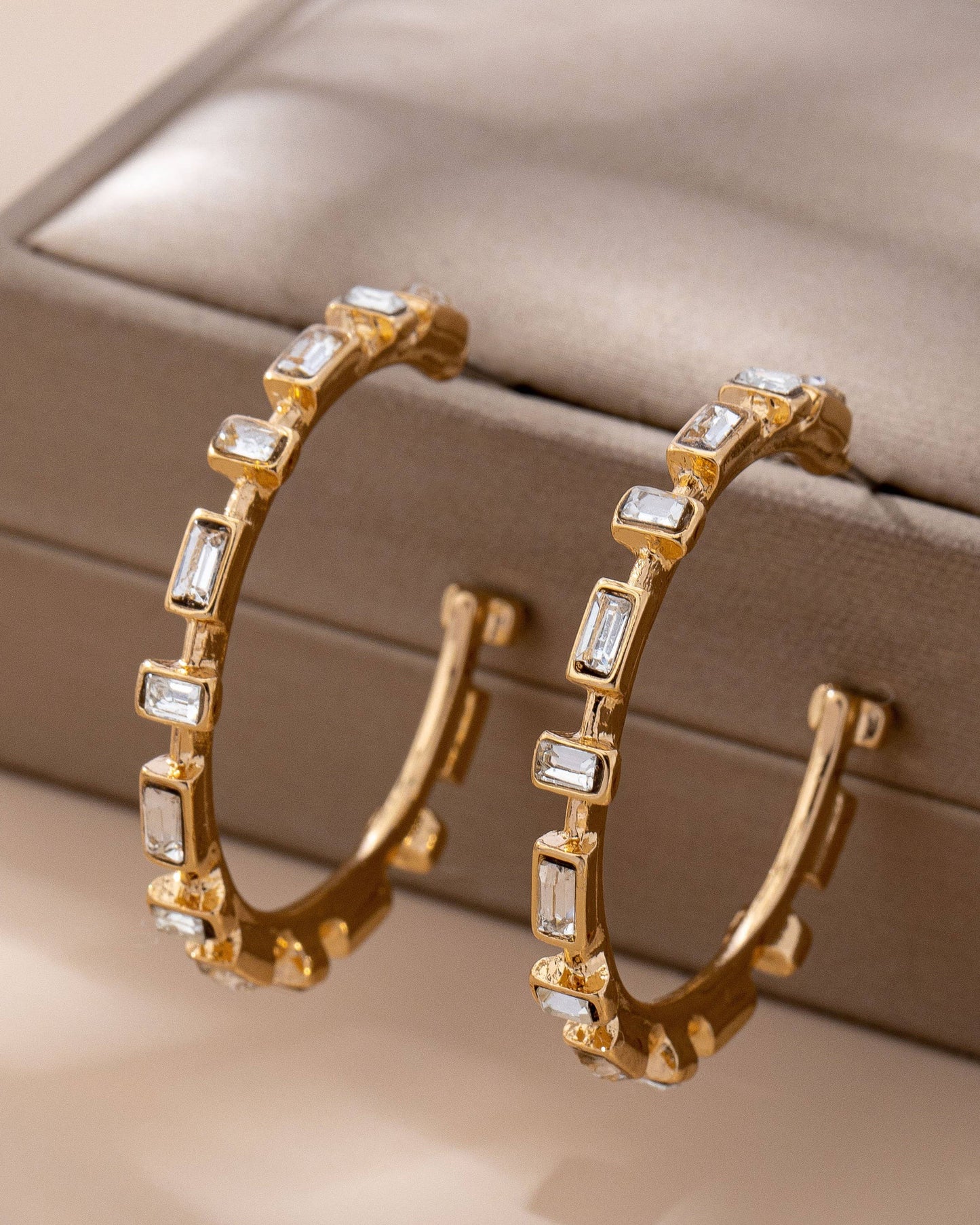 Gold hoop earrings with clear CZ gemstones on a beige jewelry box.