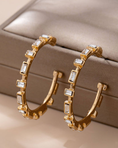 Gold hoop earrings with clear CZ gemstones on a beige jewelry box.