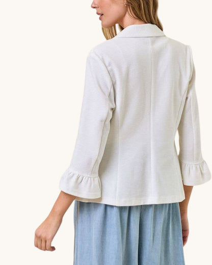 Back view of a woman wearing a white textured jacket with ruffled sleeves on a white background.
