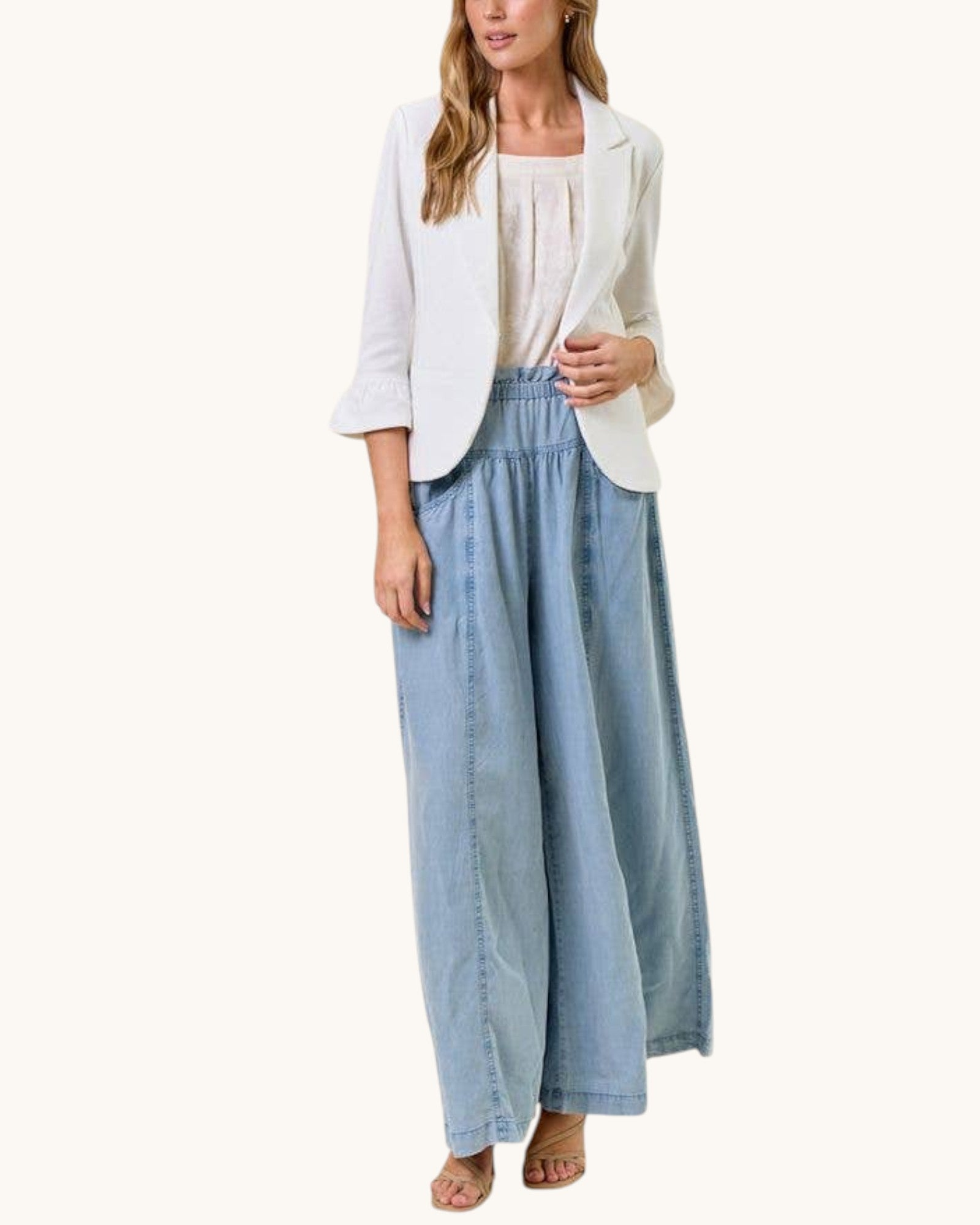 Woman wearing a white blazer and light blue pants on a white background