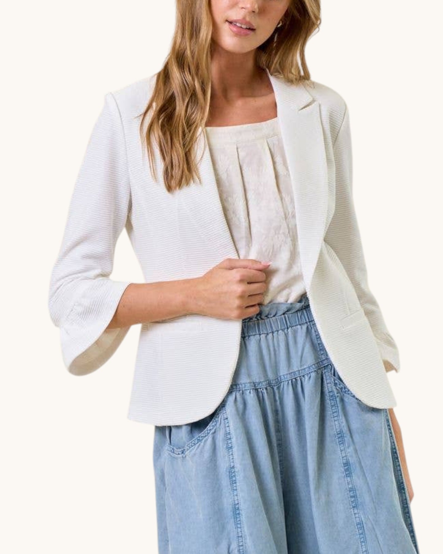 Woman wearing a white blazer over a light top and blue jeans on a white background