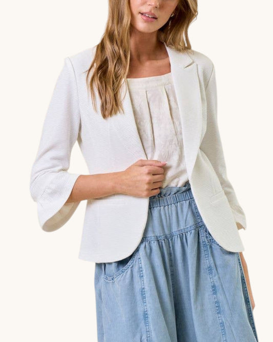 Woman wearing a white blazer over a light top and blue jeans on a white background