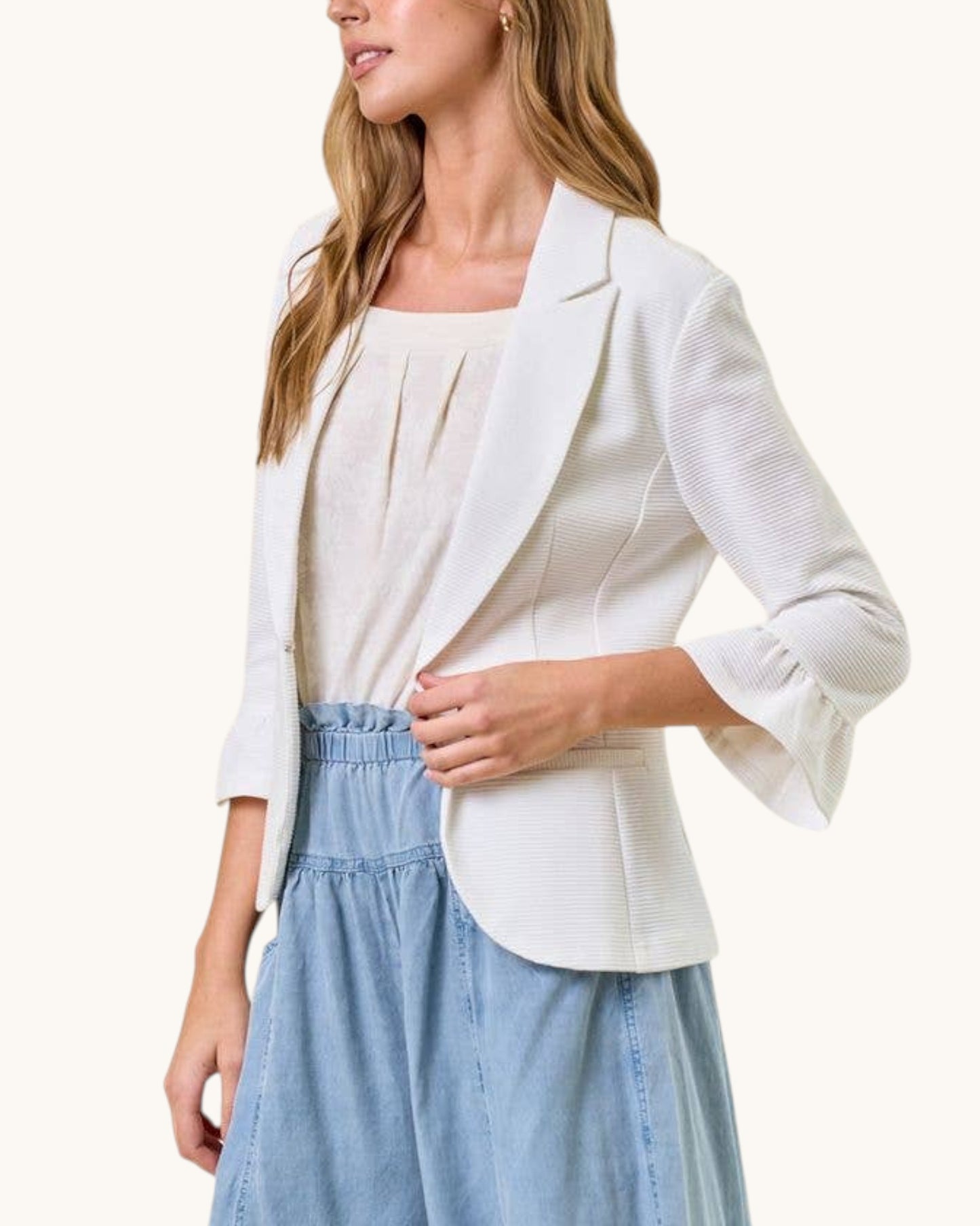Woman wearing a white blazer over a light blue dress on a white background